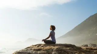 Woman meditating on rock by the sea