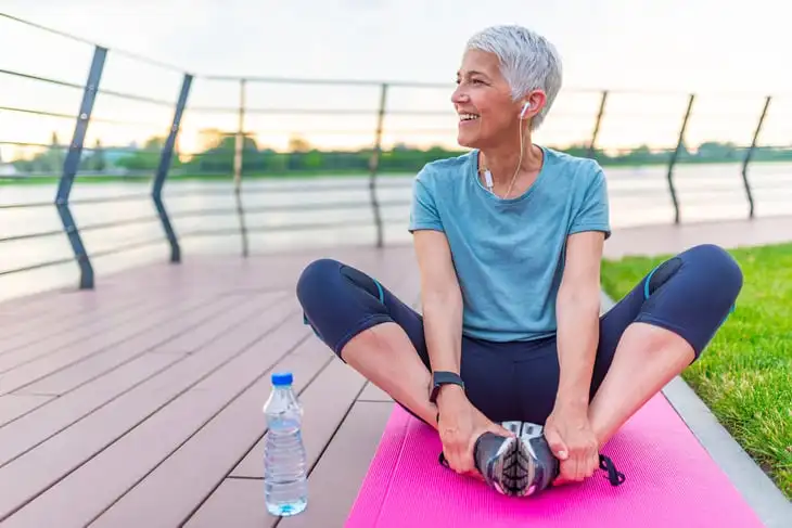 Happy senior stretching on a yoga mat outdoors