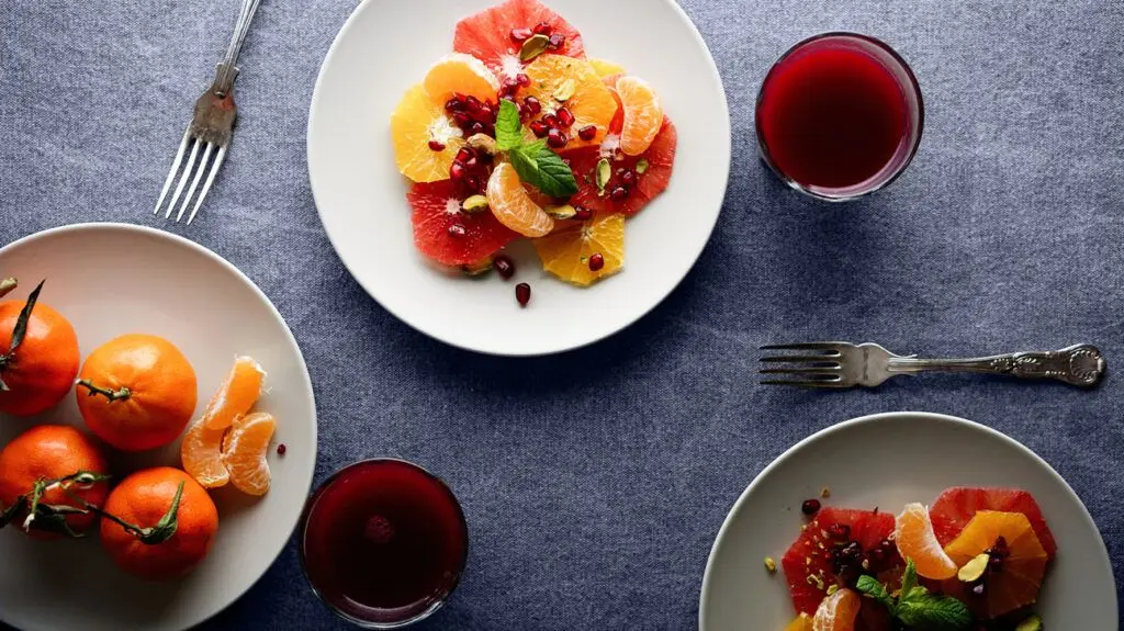 A plate full of tangerines, grapefruits, and pomegranates, fruits high in antioxidants, and a cup of fruit juice