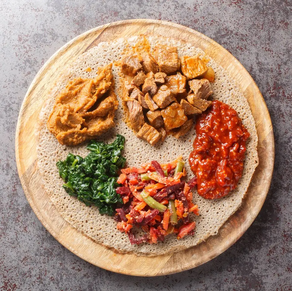 ethiopian injera topped with meat, vegetables, greens close up on the wooden board horizontal top view