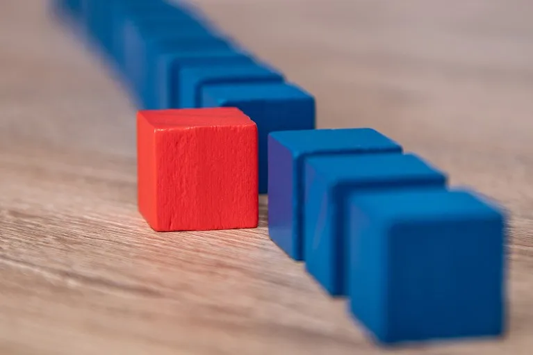 A row of blue coloured wooden blocks with a single red block standing out of line.