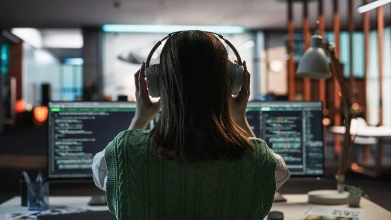 A female programmer uses headphones while working on a Desktop Computer.