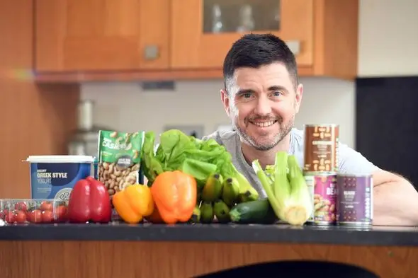 Steffan Rhys smiles for the camera with a selection of healthy foods also in shot, like beans, peppers and lettuce