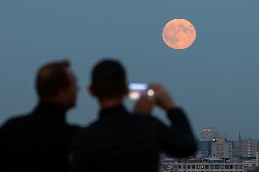 The moon rising above the Berlin skyline with two people taking a photo in the foreground