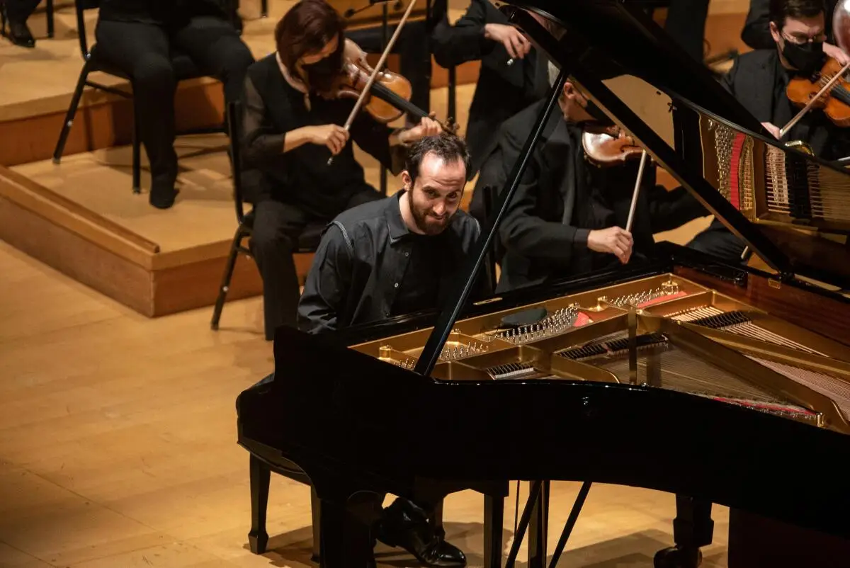 A man seated at a grand piano onstage with an orchestra