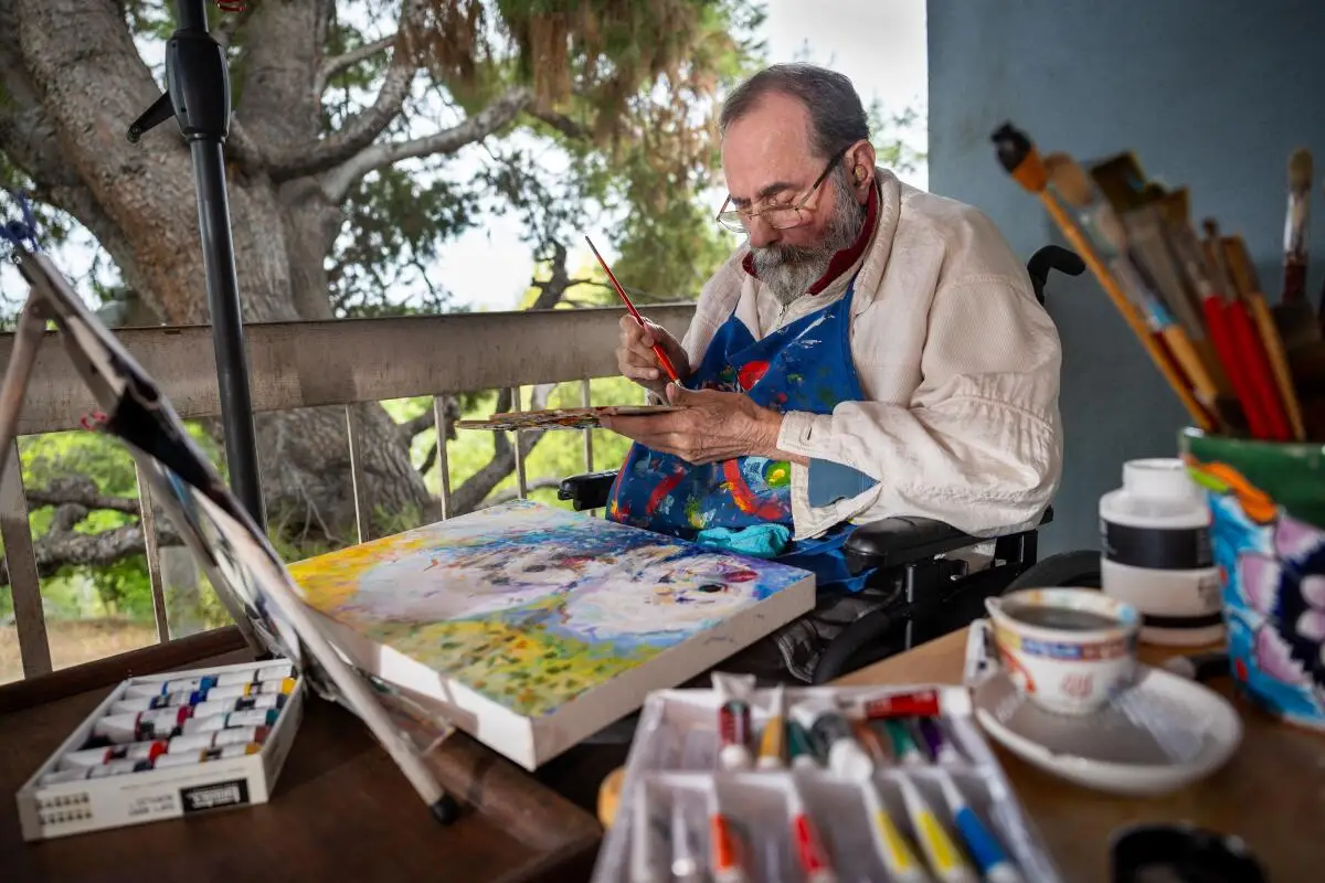 A man seated in a wheelchair, painting outdoors