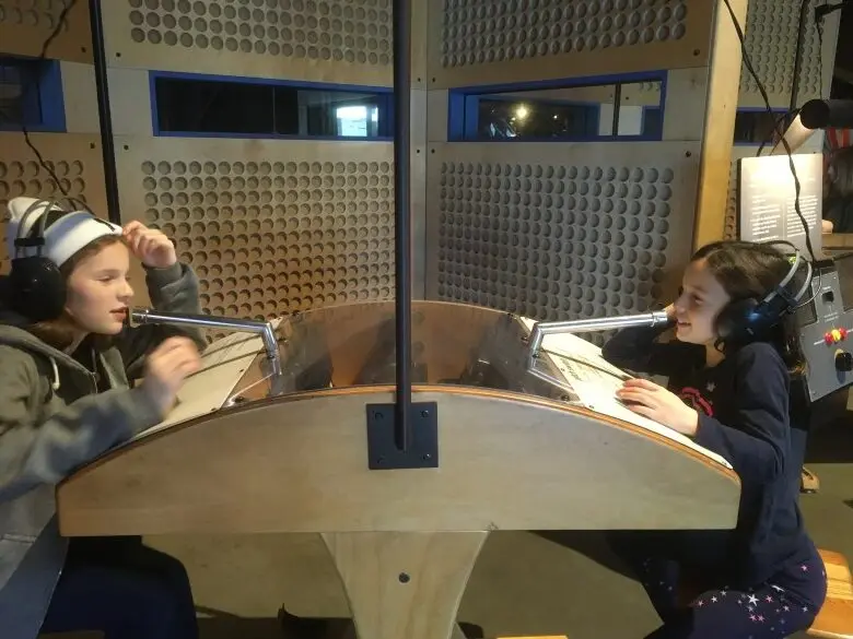 Two kids with headphones face each other at an exhibit in the Exploratorium. 