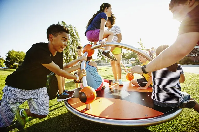 A group of kids playing on a merry go round on the playground.