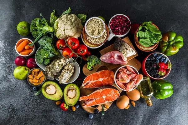 An arrangement of healthy foods in a pescatarian diet, including salmon steaks and other fish and seafood, assorted fruits, beans and other legumes, cruciferous vegetables, nuts and seeds, eggs, and olive oil.