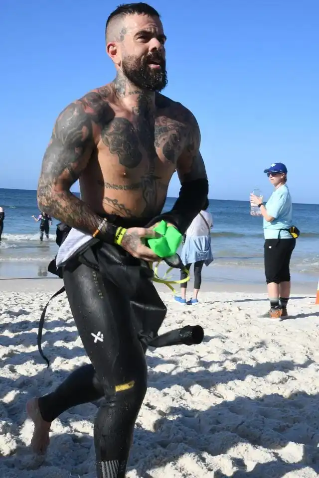 a man in a wetsuit holding a green object on a beach