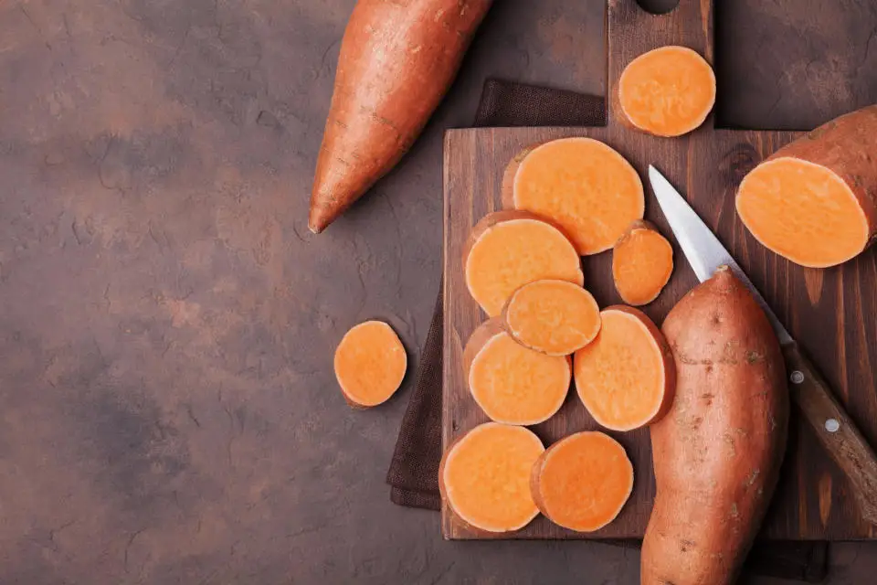 Raw sweet potatoes on wooden kitchen board top view. Organic food. Copy space for text or design.