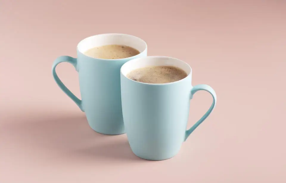 Two light blue mugs with coffee stand on a powdery background, horizontal orientation