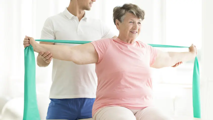 Physiatrist providing help with easing the pain of joints through exercises with a rubber strap.