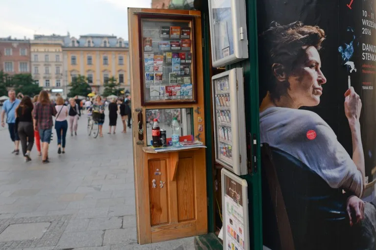 People walking past small shop selling cigarettes at Krakow's main square next to an advert featuring someone smoking a cigarette