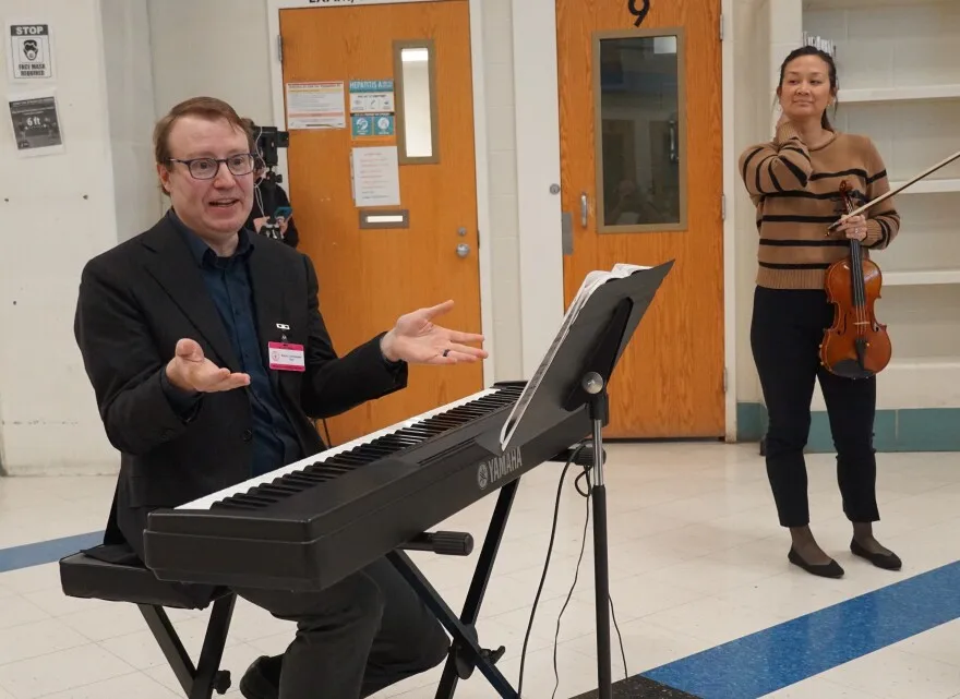 Pianist Peter Henderson provides audience members some background on a piece by composer Fritz Kreisler, as violinist Jessica Cheng Hellwege looks on.