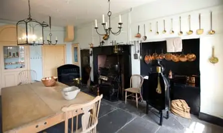 The kitchen at the Georgian House Museum showing a wooden table, candles, a fireplace and range, and cooking pots and implements