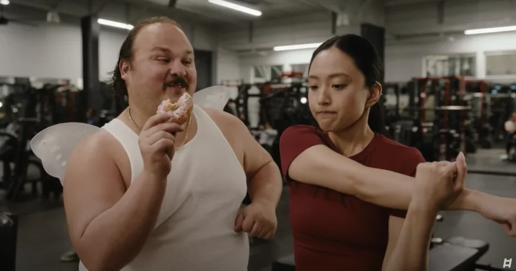 overweight man stands next to an in-shape girl inside a gym