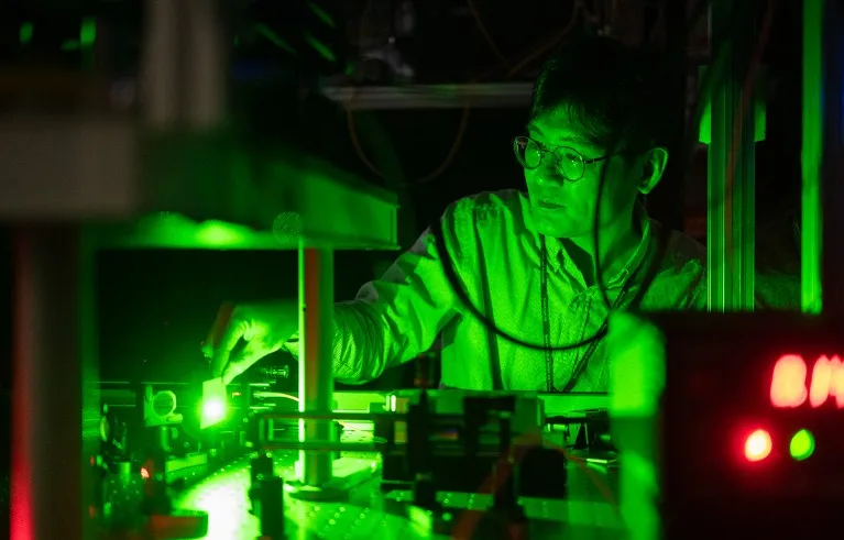 Sang-Wook Han sitting behind an optical table trying to intercept a green laser beam with a paper card.