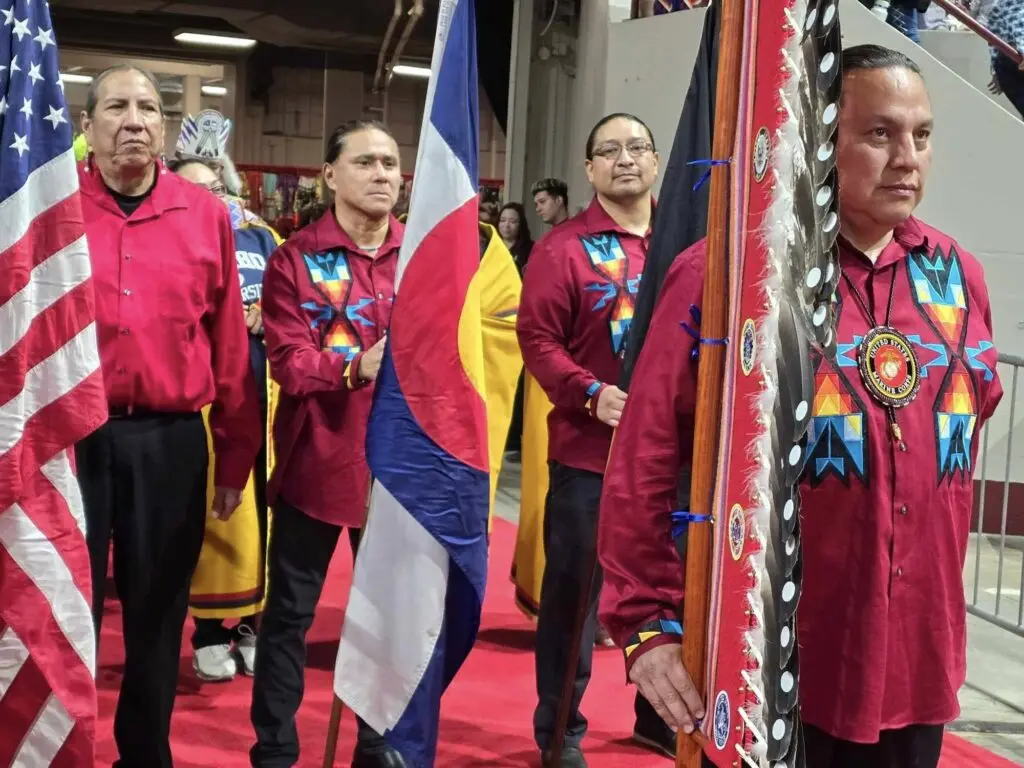 four native american men wearing red shirts and holding flags