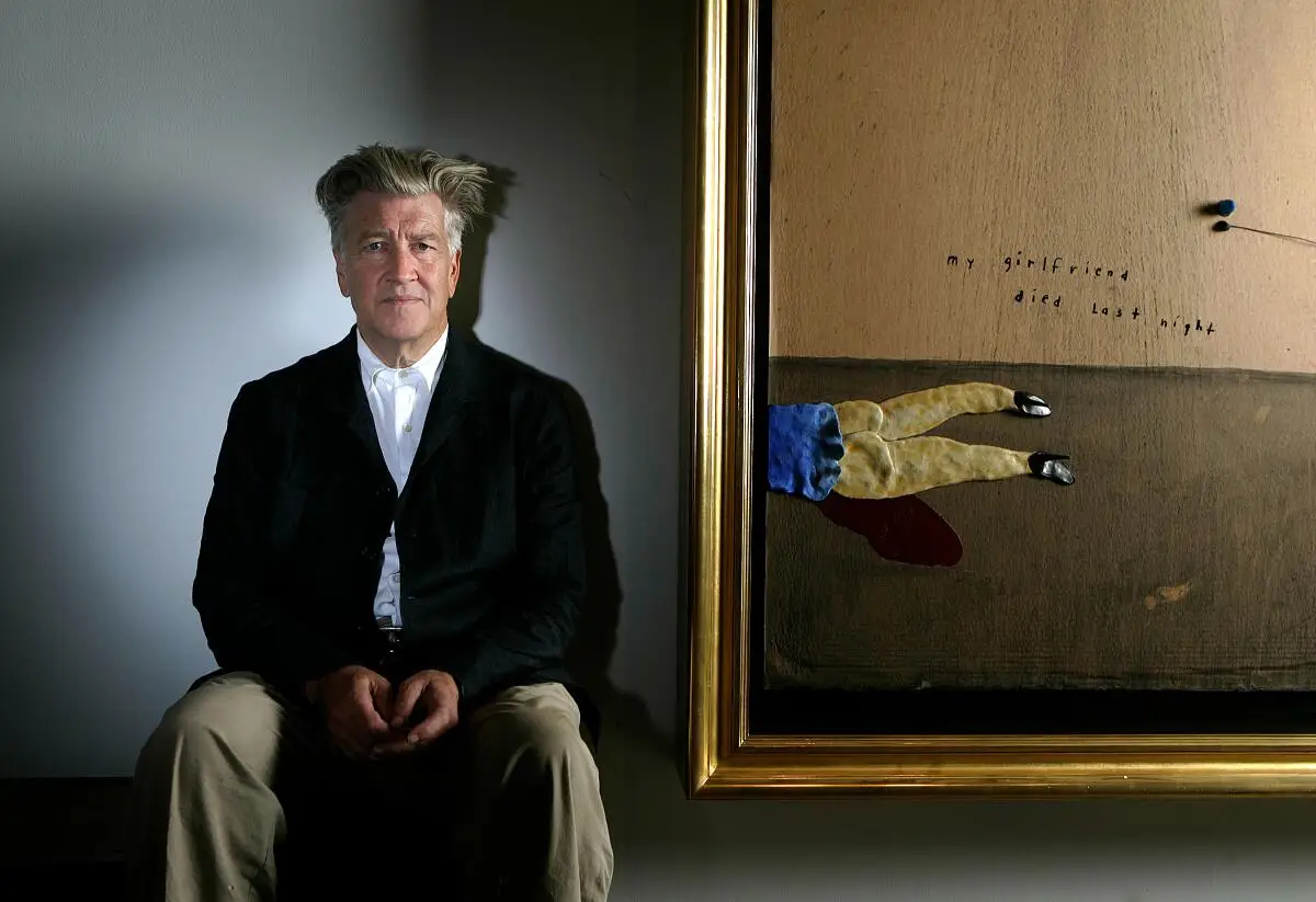 David Lynch sits near one of his paintings.