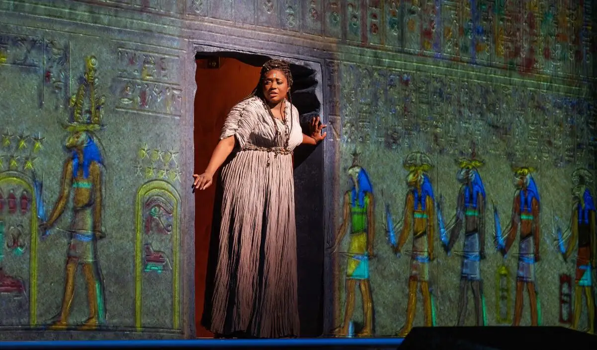 A woman walks through a door in a wall decorated with Egyptian figures and hieroglyphs