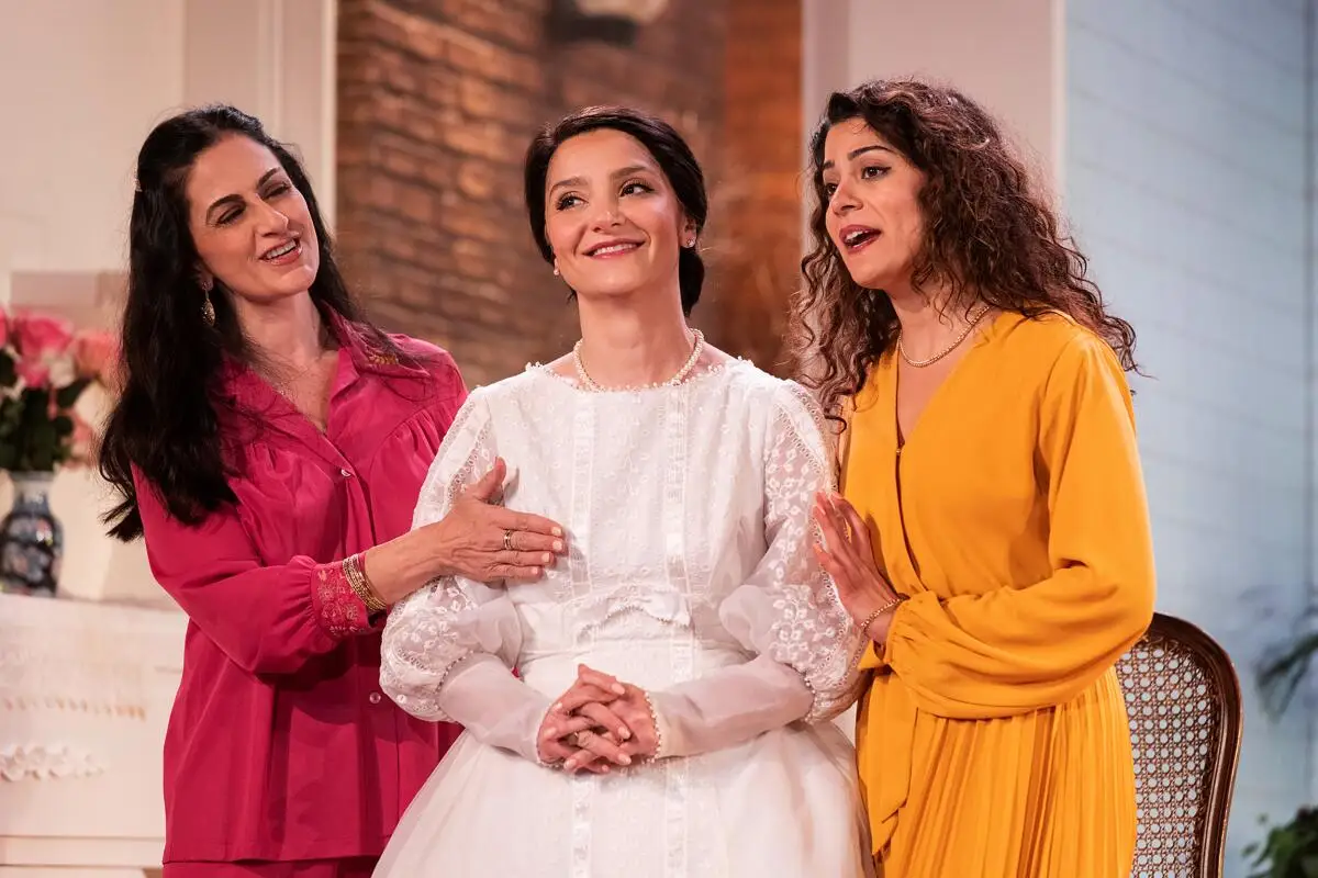 Two women, one in red, the other in orange, stand either side of a bride