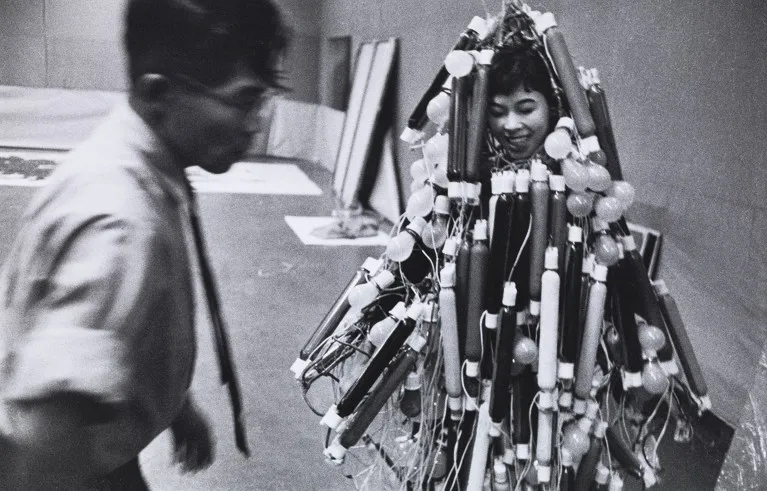 A man looks at Atsuko Tanaka wearing neon and bulb lamps