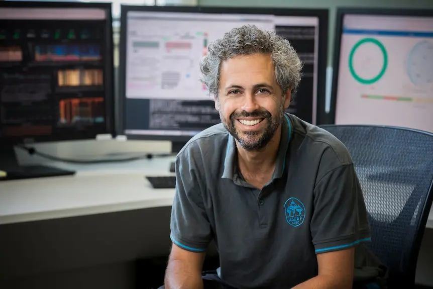 A man smiling behind computer screens.