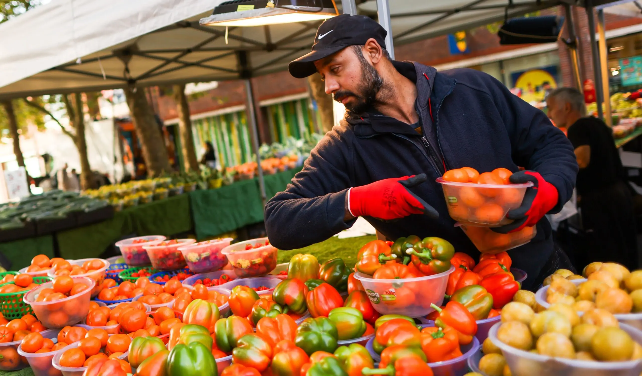 A market vendor arranging peppers and other produce at a market stall.