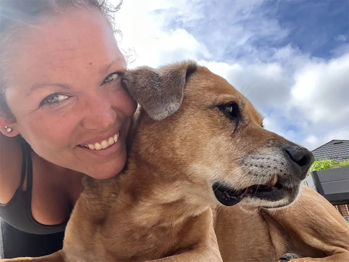 woman smiling and cuddling a beige dog