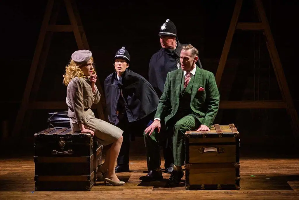 The cast of The 39 Steps at OpenStage Theatre & Company on stage sitting on vintage luggage.