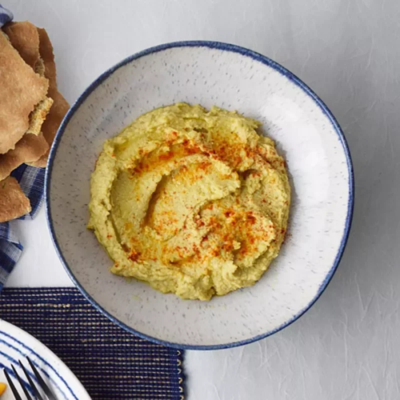 white, speckled bowl filled with hummus on countertop