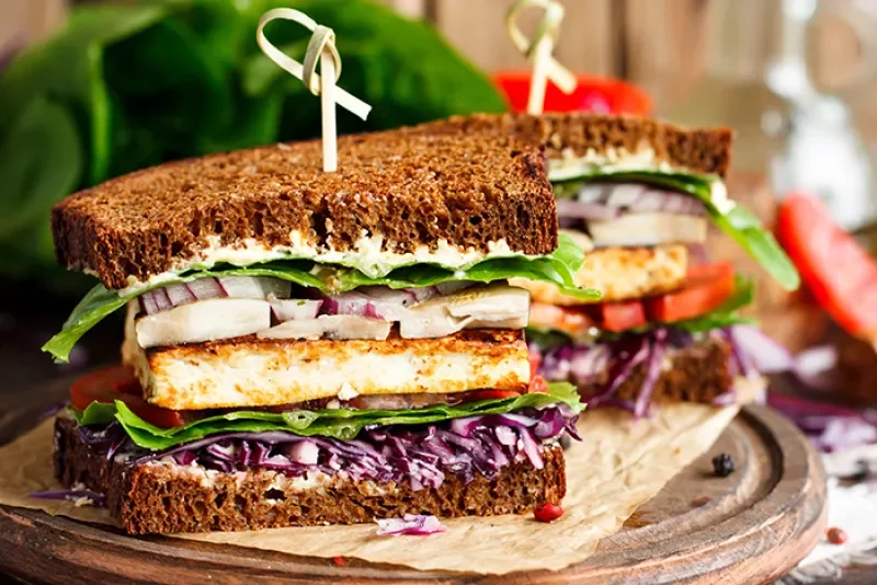 sandwich filled with veggies and tempeh cut in half on a wood cutting board