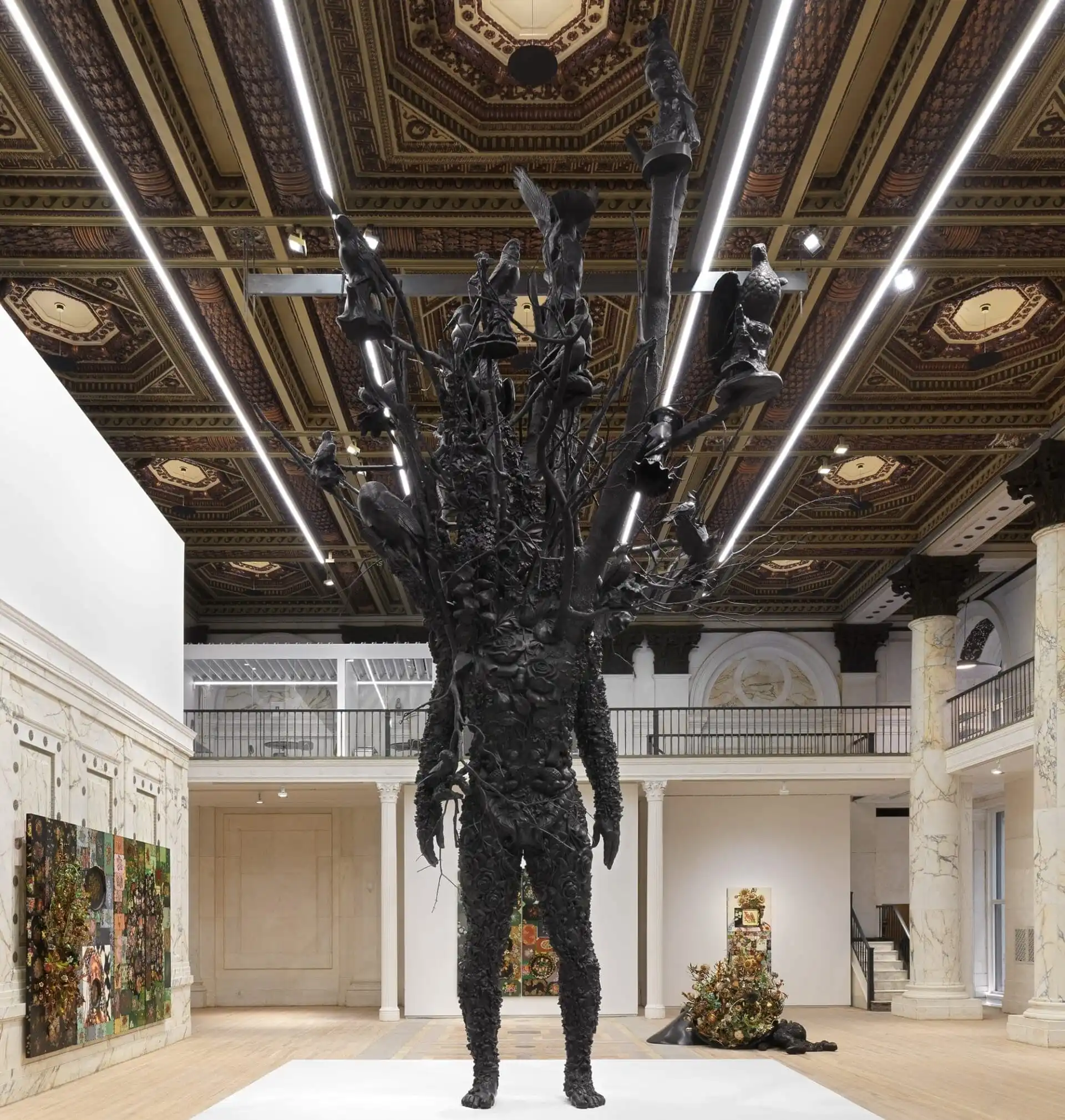 a large-scale bronze figure with branches and leaves for a head stands in a gallery