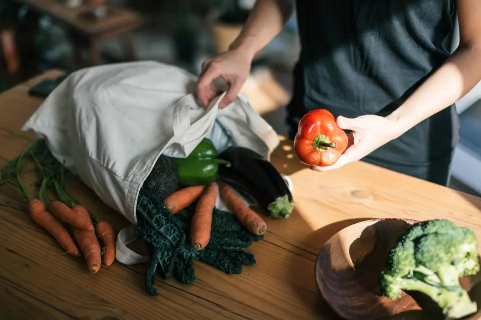 Cropped shot of young woman organising fruits and vegetables from a reusable shopping bag on the table after grocery shopping.