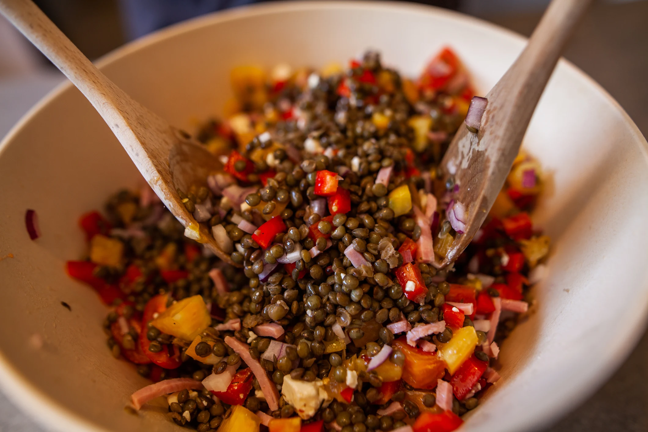 Lentil salad being mixed in a bowl with wooden spoons.