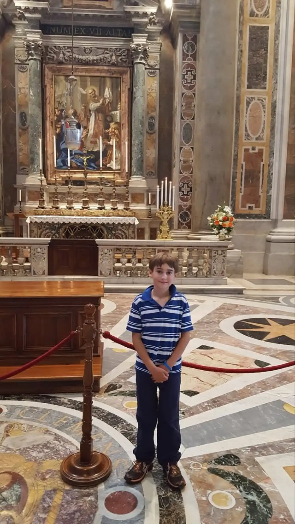 A smiling boy stands in front of a painting in a church.