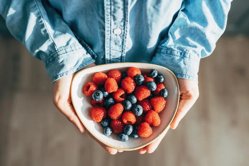 A woman holds a plate of fruits and berries in her hands