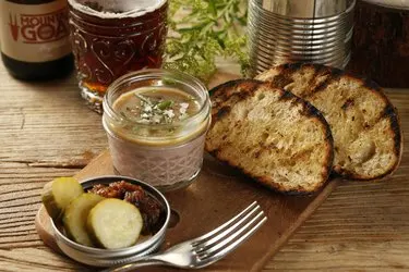 liver pate with pickles and two toasted baguette slices on a wooden serving board