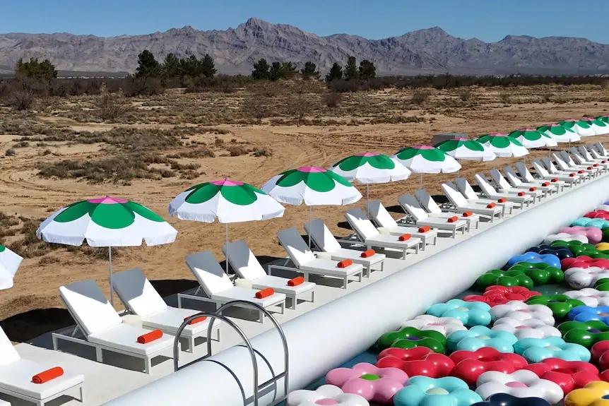 Outdoor pool filled with brightly coloured flower-shaped floaties, with mountains and blue sky behind it.