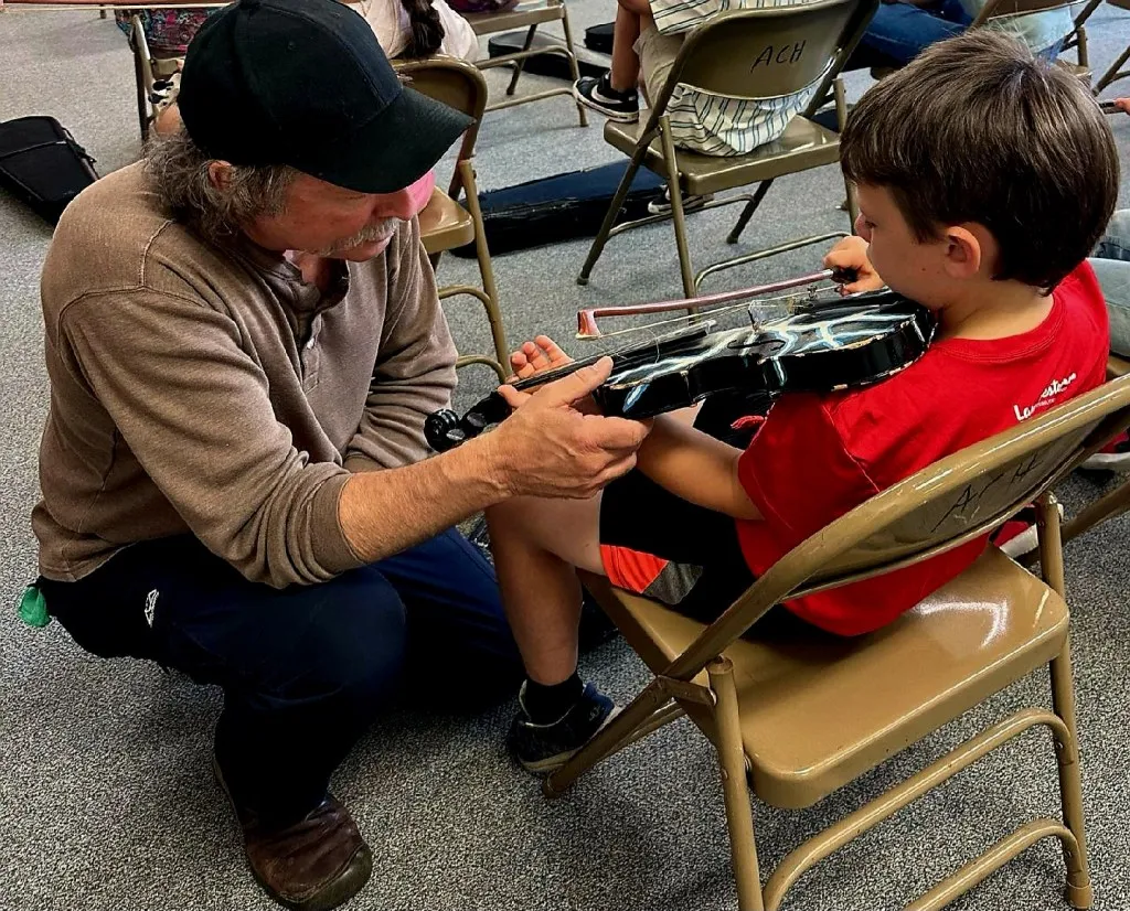 Kelly Thibodeaux, a fiddler from Oakridge, gives a youngster at A.C. Houghton Elementary School in Irrigon a chance to try his hand at the fiddle in a class sponsored by Art Center East's Artists in Rural School program. Photo courtesy: Art Center East