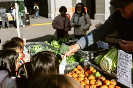 a man working a farmers market stand hands kids produce