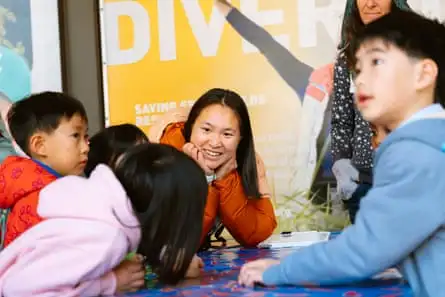 A smiling woman interacts with elementary schoolers