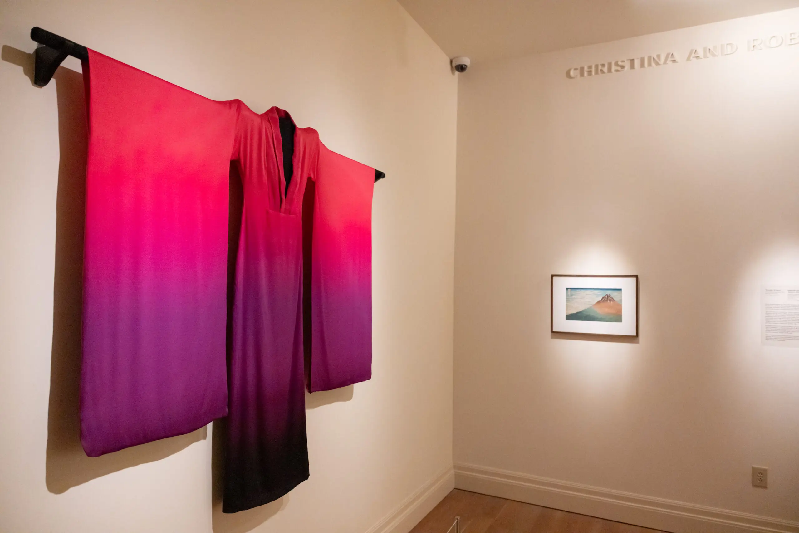 A gradient purple and pink kimono hung next to a Japanese woodblock print of a mountain