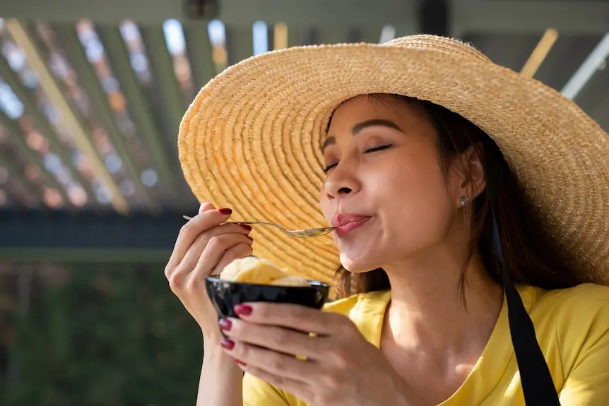 Woman in straw hat eating a tub of vanilla ice cream.