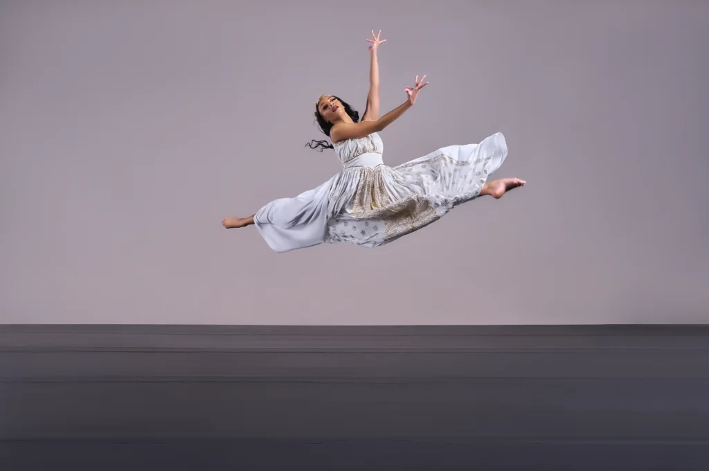 A woman in a white dress leaps on stage during the Cleo Parker Robinson Dance Black Orpheus performance.