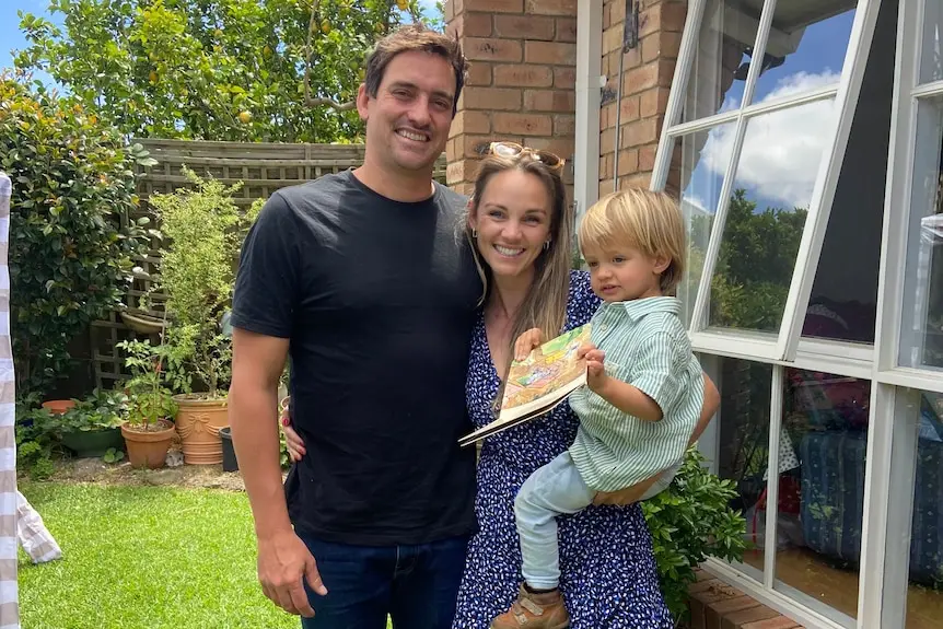 A woman and man smiling. The woman is holding a toddler.