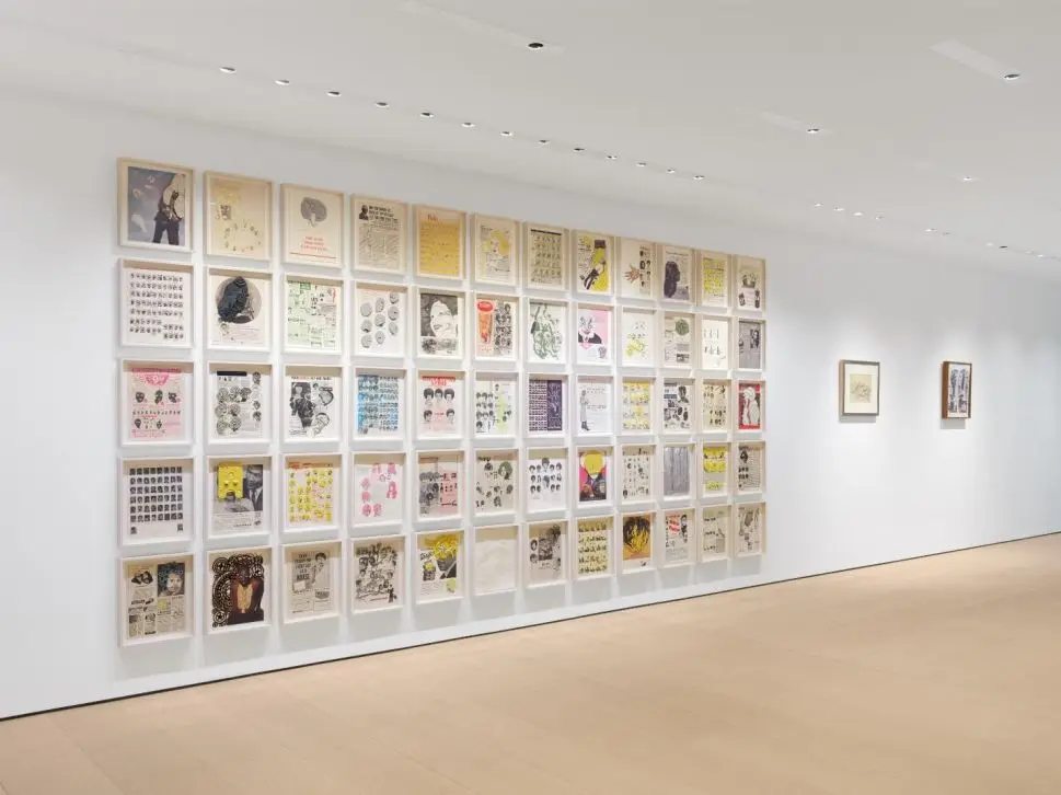 A gallery wall features a grid display of framed vintage-style illustrations and collages, arranged neatly in rows, with bright lighting illuminating the space.