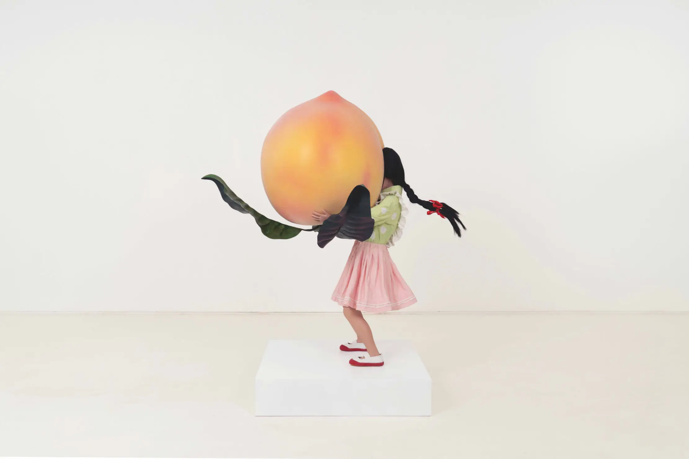 Sculpture by Renee Jin shows a young girl with her face buried in an oversized peach she is holding.