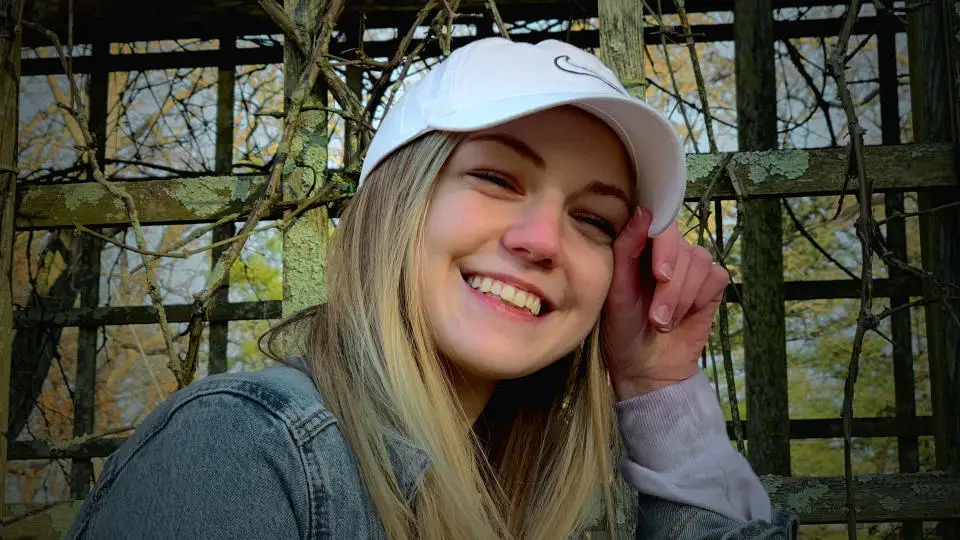 A close-up portrait of Gabby Petito in a white baseball cap looking cheerful.